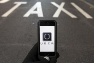 Photo illustration of logo of car-sharing service app Uber on a smartphone over a reserved lane for taxis in a street in Madrid